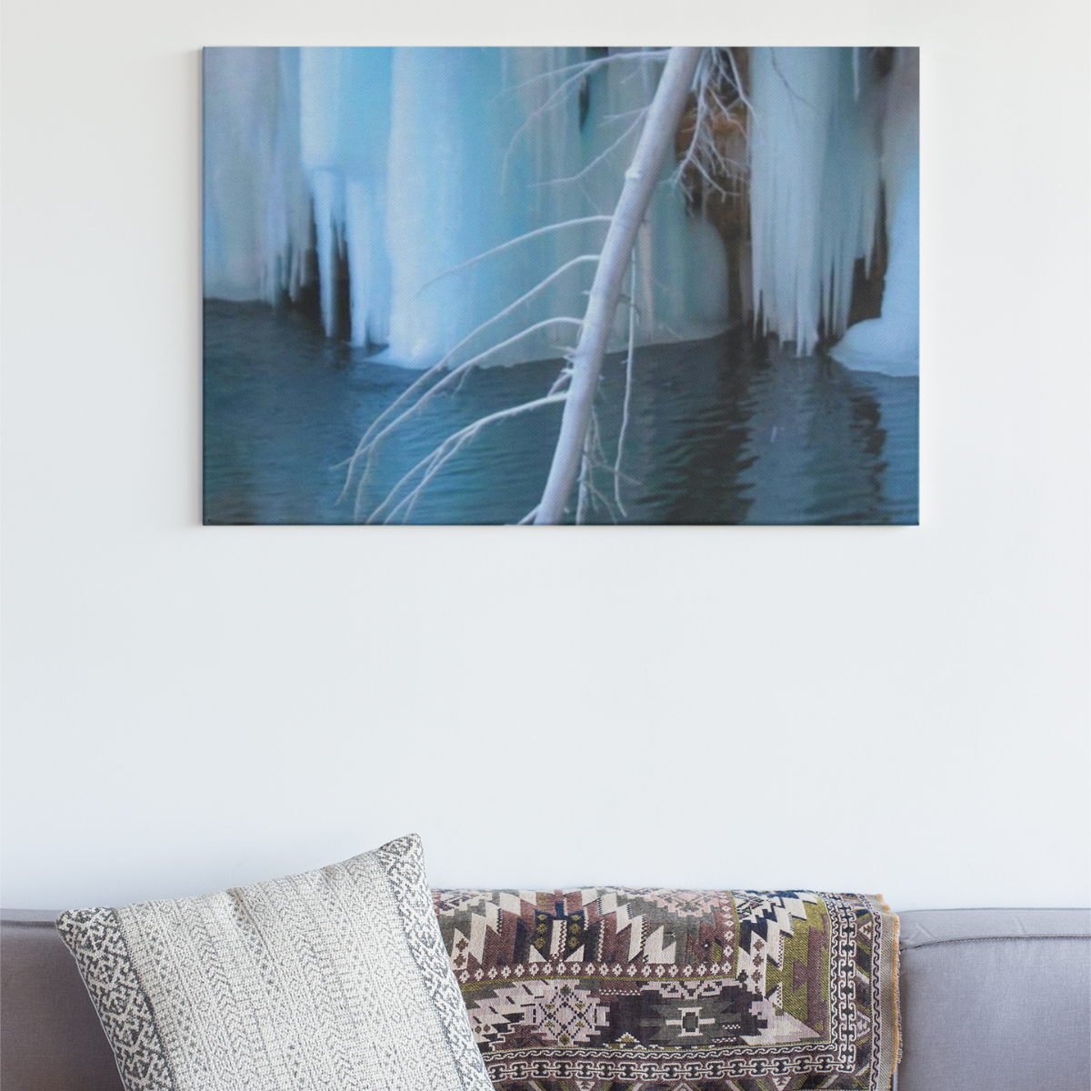 Gray sofa with decorative pillows and a blanket, featuring a large wall art of icy landscape.
